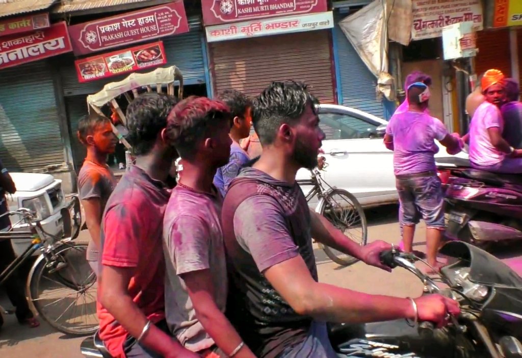 ホーリー祭りで色に染まったバイクに3人乗りをしている男性